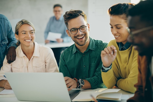 Heureux étudiant s'amusant en utilisant un ordinateur portable avec ses amis dans la salle de classe