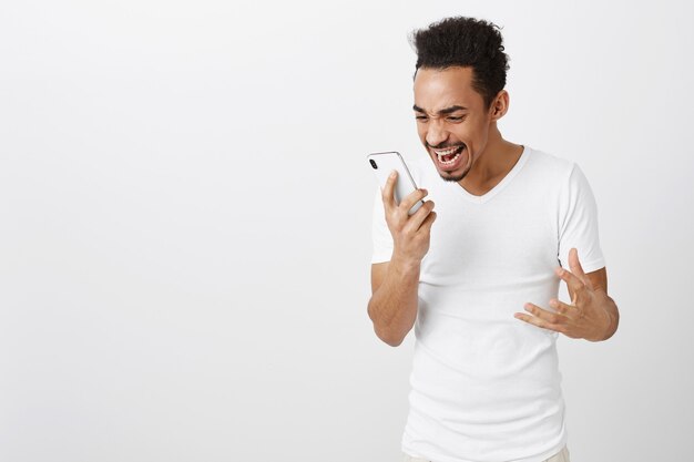 Heureux et excité triomphant de l'homme afro-américain regardant l'écran du téléphone mobile avec le visage ravi, se réjouissant