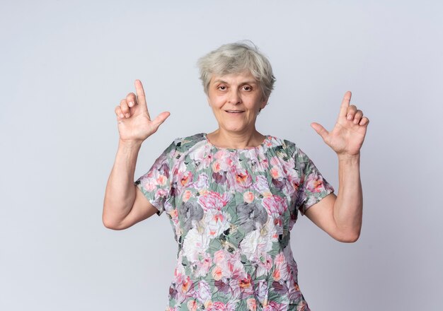 Heureux femme âgée pointe avec deux mains isolé sur un mur blanc