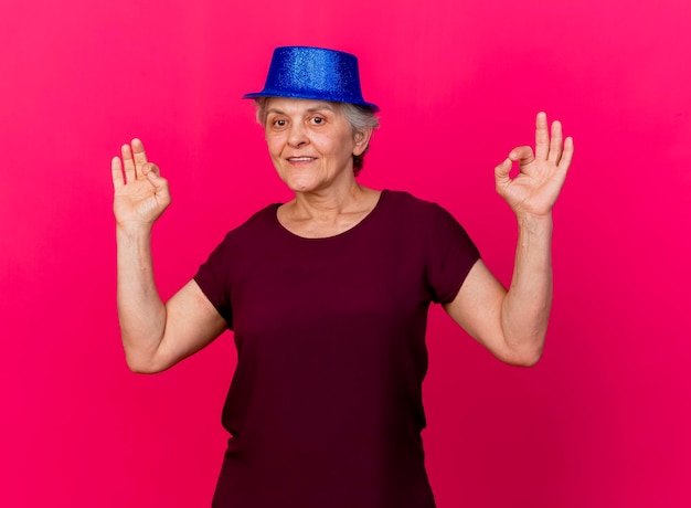 Heureux femme âgée portant des gestes de chapeau de fête ok signe de la main avec deux mains sur rose