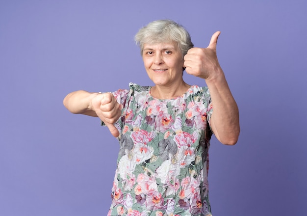 Heureux femme âgée pouces vers le haut et pouces vers le bas isolé sur mur violet