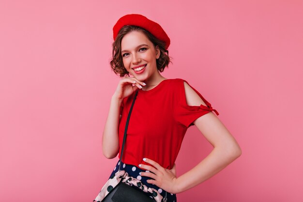 Heureux femme blanche en tenue française élégante posant avec un sourire heureux. Portrait de fille debonair en vêtements rouges.