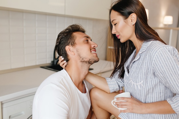 Heureux femme brune en pyjama buvant du café et caressant les cheveux de son mari