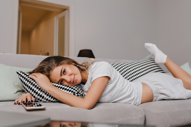 Heureux femme en chaussettes allongé sur un canapé avec des coussins et souriant doucement