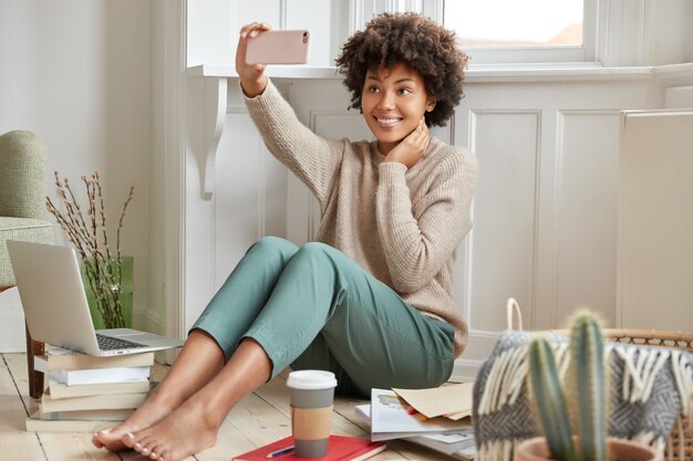 Heureux femme métisse avec une coiffure afro, pose au téléphone portable pour faire selfie