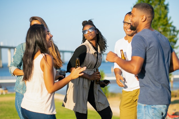 Heureux Femmes Et Hommes Qui Dansent Dans Le Parc En Soirée. Joyeux Amis Se Détendre Avec De La Bière Pendant Le Coucher Du Soleil. Concept De Loisirs