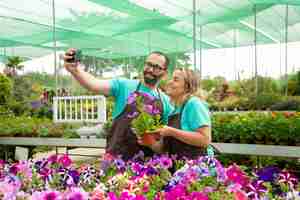 Photo gratuite heureux fermiers prenant selfie avec une plante de pétunia en fleurs