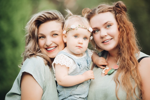 Photo gratuite heureux avec une fille qui rit posant ensemble à l'extérieur sur fond d'arbre vert. mère et père souriants tenant des enfants appréciant la parentalité