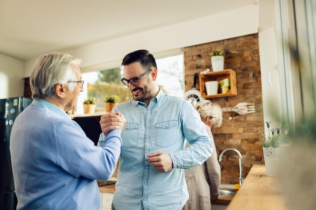 Heureux fils adulte et son père mature se tenant la main tout en se saluant dans la cuisine