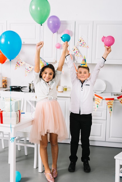 Heureux garçon et fille debout dans la cuisine tenant des ballons colorés à la main
