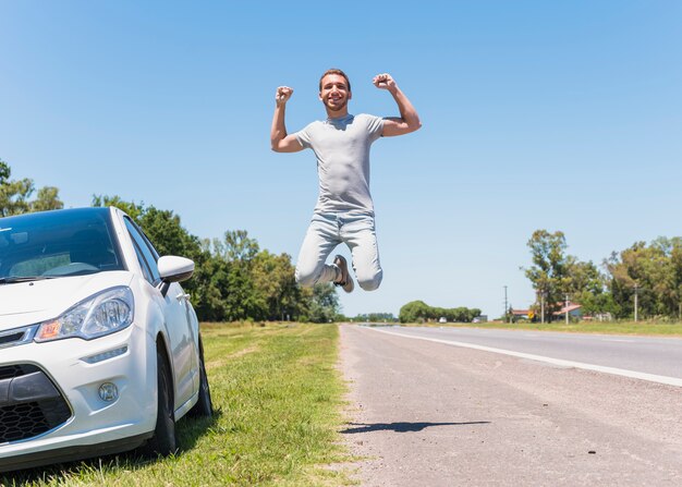 Heureux garçon sautant sur la route à côté de la voiture