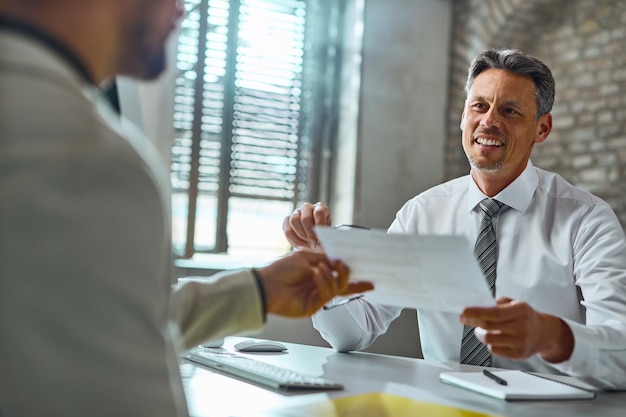 Heureux homme d'affaires d'âge moyen parlant avec un candidat et prenant son CV lors d'un entretien d'embauche au bureau