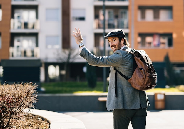 Photo gratuite heureux homme d'affaires avec le bras levé saluant quelqu'un en marchant dans la rue.