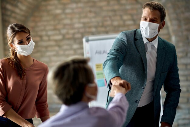 Heureux homme d'affaires avec masque facial saluant son collègue et se cognant le poing lors d'une réunion pendant l'épidémie de coronavirus