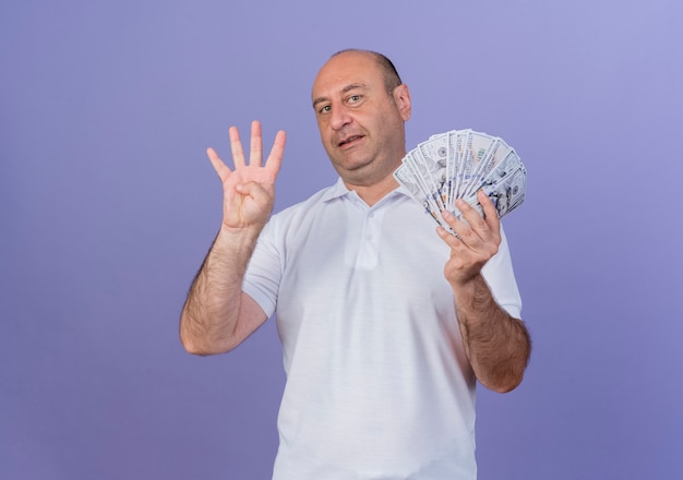 Heureux homme d'affaires mature occasionnel tenant de l'argent et montrant quatre avec la main isolé sur fond violet avec copie espace