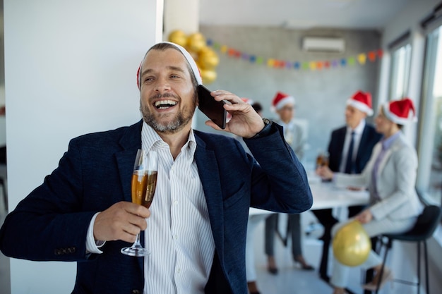 Photo gratuite heureux homme d'affaires parlant au téléphone tout en buvant du champagne lors de la fête du nouvel an au bureau