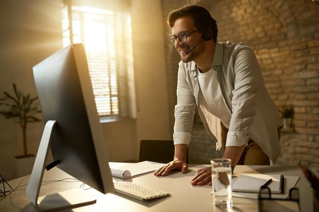 Photo gratuite heureux homme d'affaires portant un casque lors d'un appel vidéo sur un ordinateur de bureau au bureau