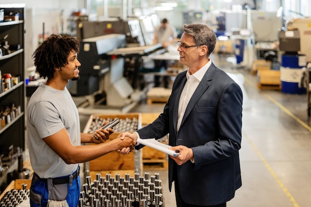 Heureux homme d'affaires saluant un travailleur de l'acier afro-américain lors de la visite d'une installation industrielle