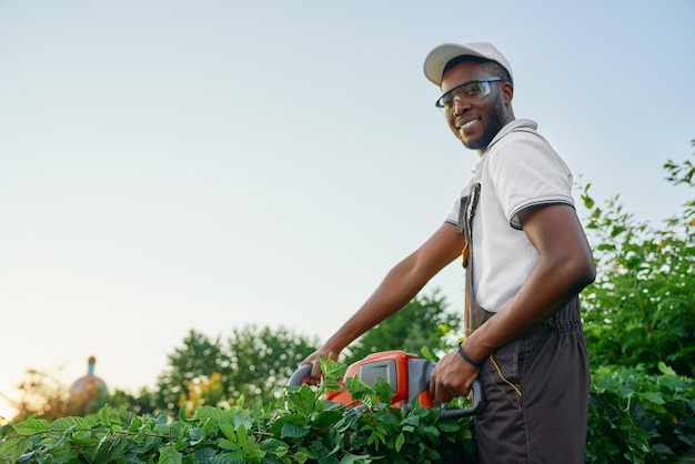 Photo gratuite heureux homme africain coupant les buissons avec une tondeuse à essence