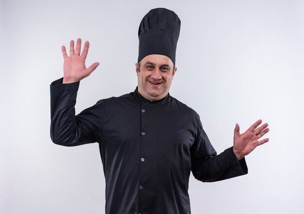 Heureux homme d'âge moyen cuisinier en uniforme de chef se propage les mains sur un mur blanc isolé