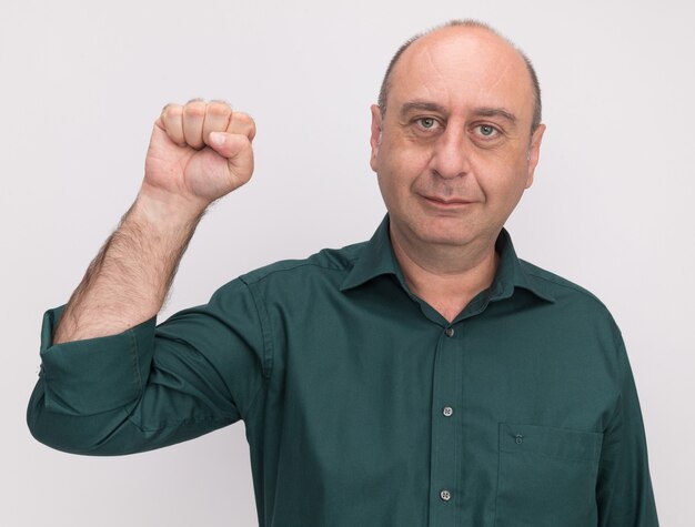 Heureux homme d'âge moyen portant un t-shirt vert tenant le poing isolé sur un mur blanc