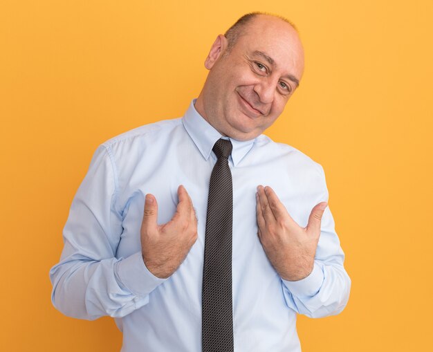 Photo gratuite heureux homme d'âge moyen de la tête inclinable portant un t-shirt blanc avec des points de cravate à lui-même isolé sur un mur orange