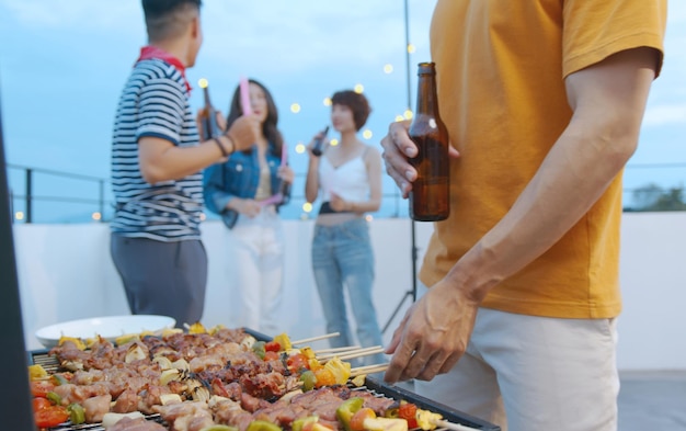 Heureux homme asiatique avec des amis lors d'un dîner barbecue et savourant un repas ensemble