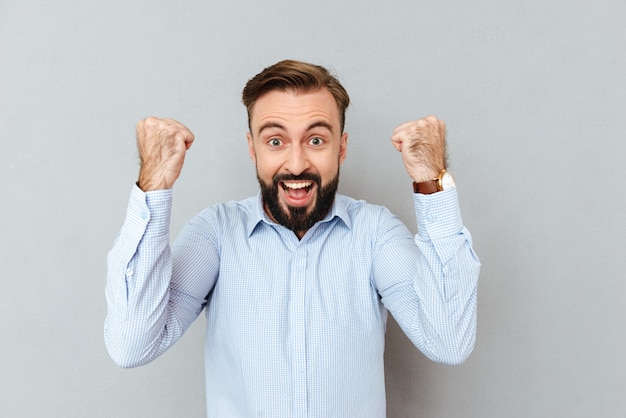 Heureux homme barbu hurlant dans des vêtements d'affaires regardant la caméra