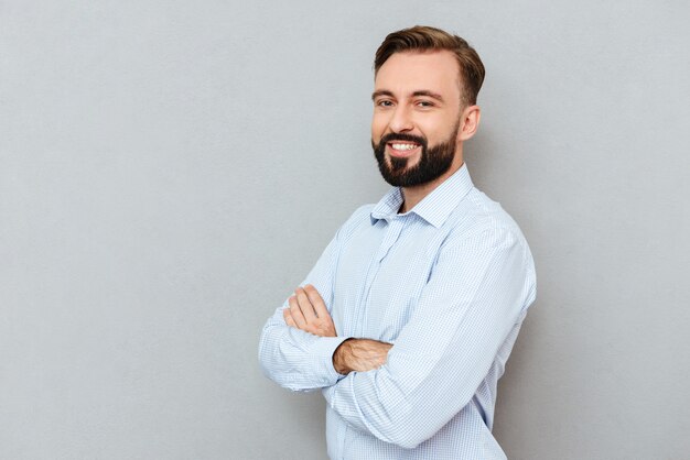 Heureux homme barbu en vêtements d'affaires avec les bras croisés