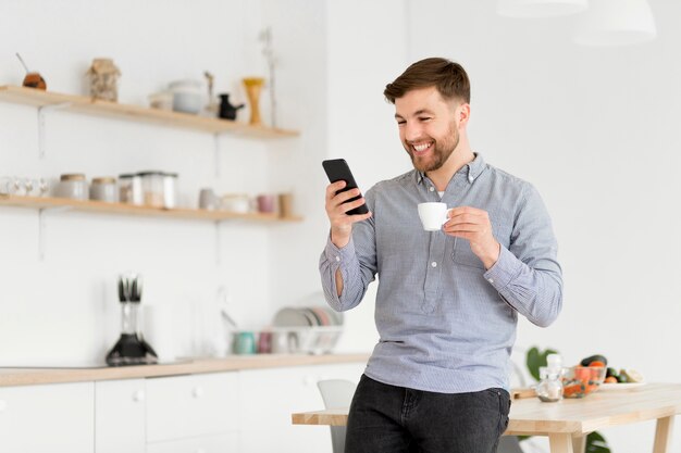 Heureux homme buvant du café tout en vérifiant le mobile