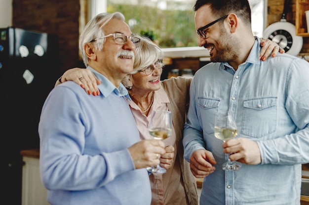 Heureux homme buvant du vin avec ses parents matures dans la cuisine L'accent est mis sur une femme âgée