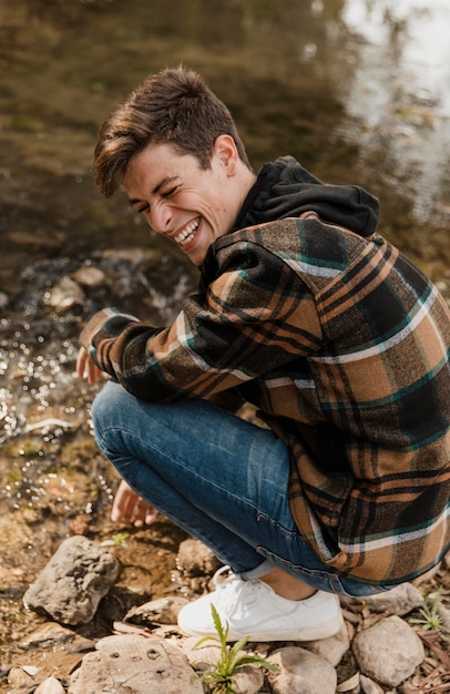 Photo gratuite heureux homme de camping dans la forêt assis au bord de la rivière