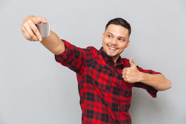 Heureux homme décontracté en chemise à carreaux faisant selfie