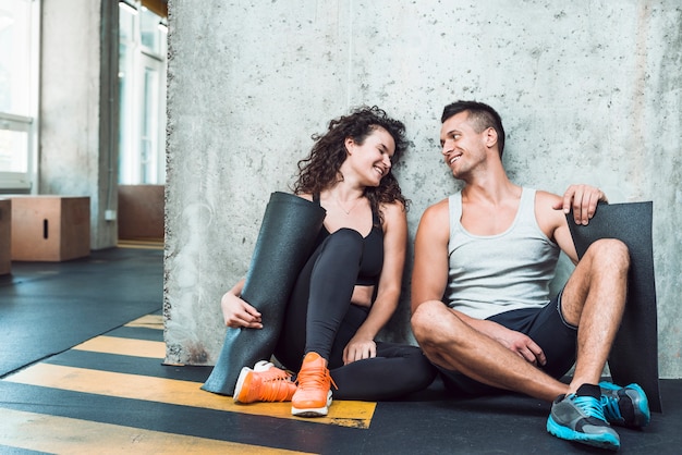 Heureux homme et femme avec tapis d&#39;exercice assis dans une salle de sport