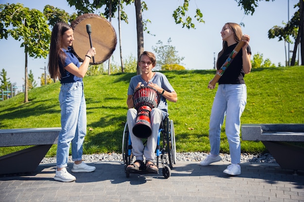 Heureux homme handicapé en fauteuil roulant, passer du temps avec des amis à jouer de la musique instrumentale en direct à l'extérieur.