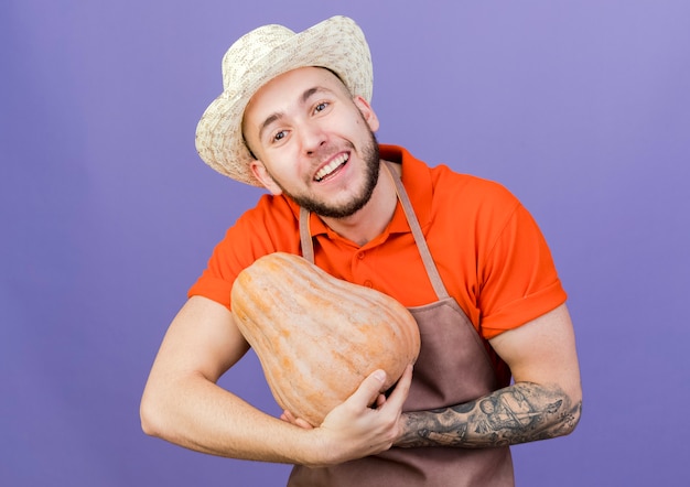 Heureux homme jardinier portant chapeau de jardinage détient citrouille