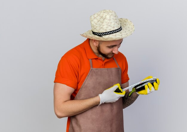 Heureux homme jardinier portant chapeau de jardinage mesure l'aubergine avec un ruban à mesurer