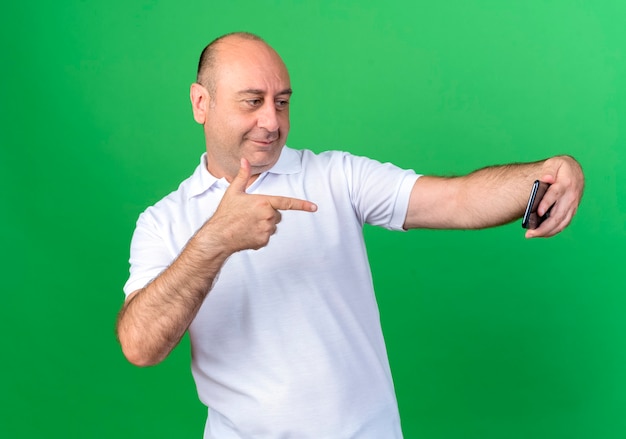 Heureux homme mûr occasionnel prendre un selfie et des points au téléphone isolé sur fond vert