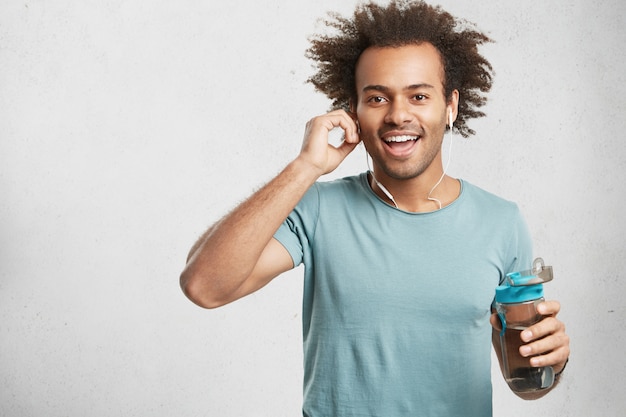 Heureux homme positif avec chaume sourit joyeusement, écoute de la musique dans les écouteurs