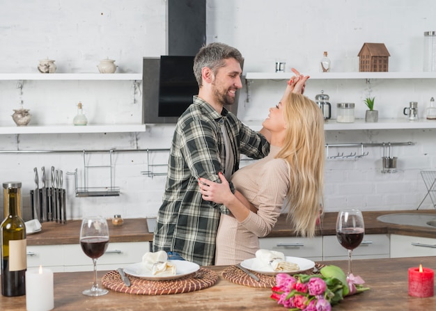 Heureux homme qui danse avec une femme blonde près de la table dans la cuisine