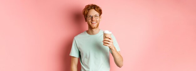 Heureux homme roux dans des verres et tshirt boire du café et souriant appréciant la pause déjeuner tenant tak