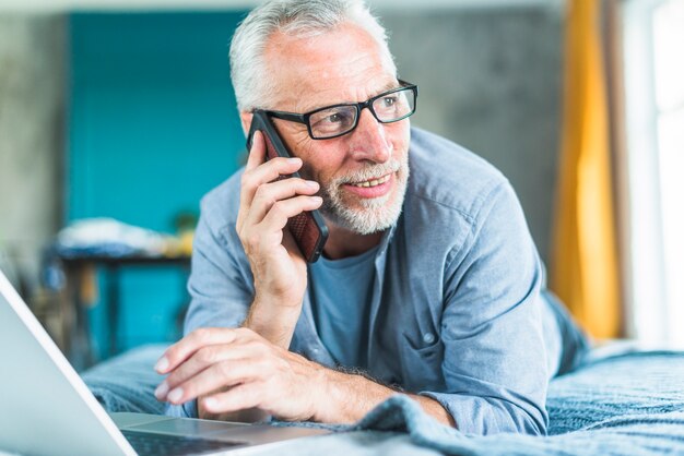 Heureux homme senior parler sur téléphone intelligent en détournant les yeux