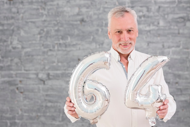 Photo gratuite heureux homme senior tenant un ballon en feuille d'argent à son 64e anniversaire