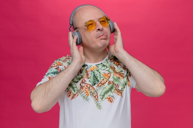 Heureux homme slave adulte avec des lunettes de soleil et des écouteurs sort sa langue et regarde de côté