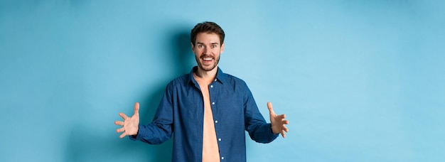 Photo gratuite heureux homme souriant montrant un objet de grande taille façonnant une grande chose et regardant étonné debout sur ba bleu