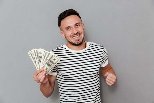 Heureux homme en t-shirt tenant de l'argent et regardant la caméra