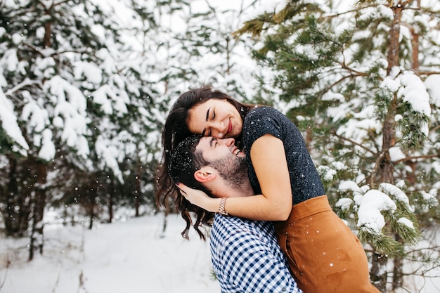 Heureux homme tenant une femme dans les bras dans la forêt d&#39;hiver