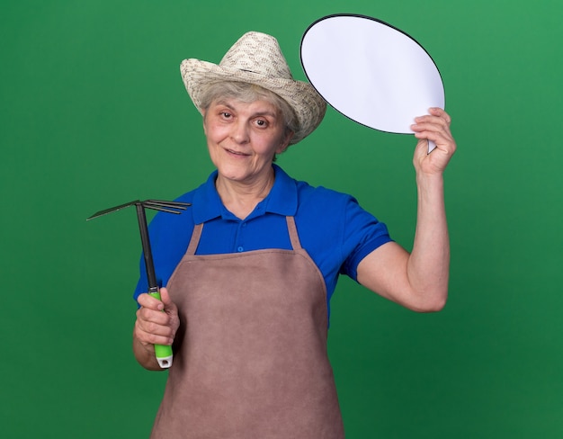 Heureux jardinier femme âgée portant un chapeau de jardinage tenant un râteau et une bulle de dialogue