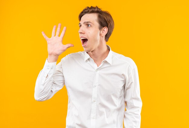 Heureux jeune beau mec vêtu d'une chemise blanche appelant quelqu'un isolé sur un mur orange