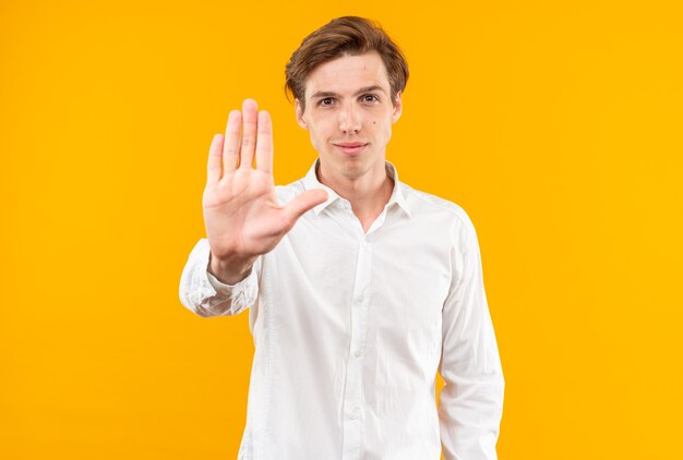 heureux jeune beau mec vêtu d'une chemise blanche montrant un geste d'arrêt isolé sur un mur orange